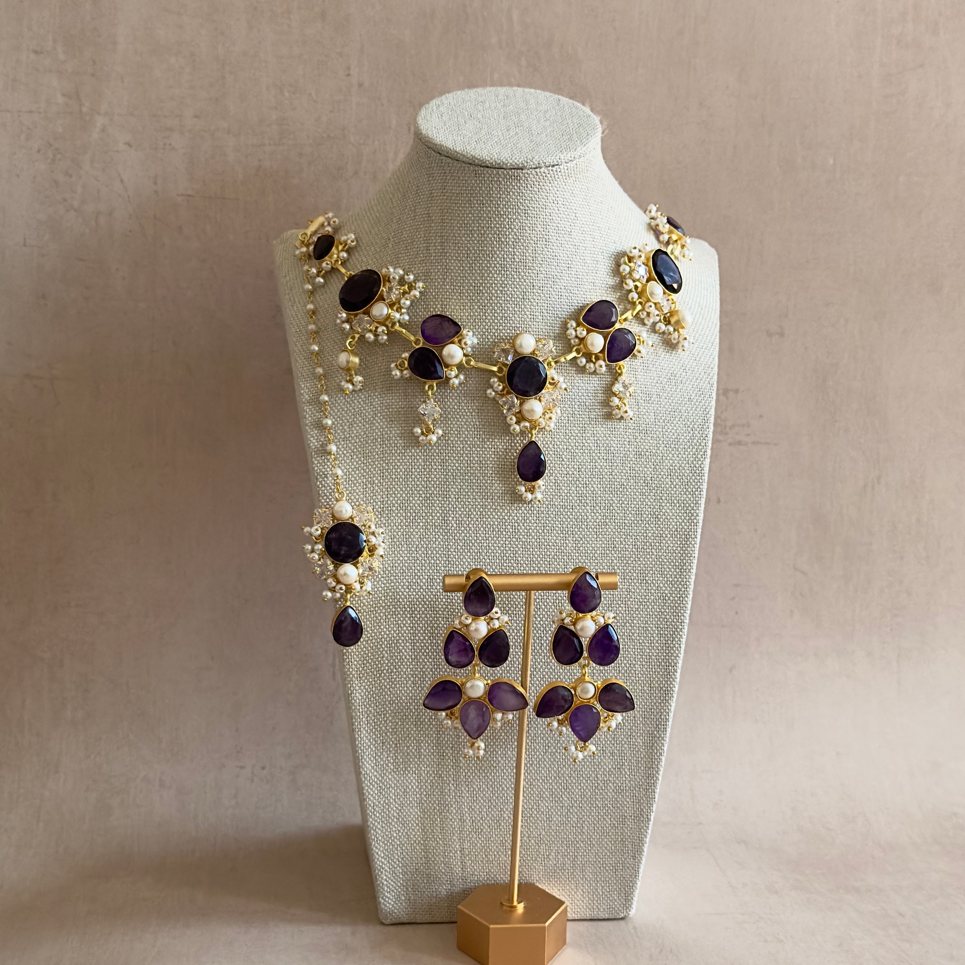 Elevate your style with our Bali Purple Necklace Set! Adorned with hand cut amethyst stones, freshwater pearls, and sparkling cubic zirconia, this set radiates beauty and sophistication. Complete with matching earrings and tikka. Perfect for any occasion.