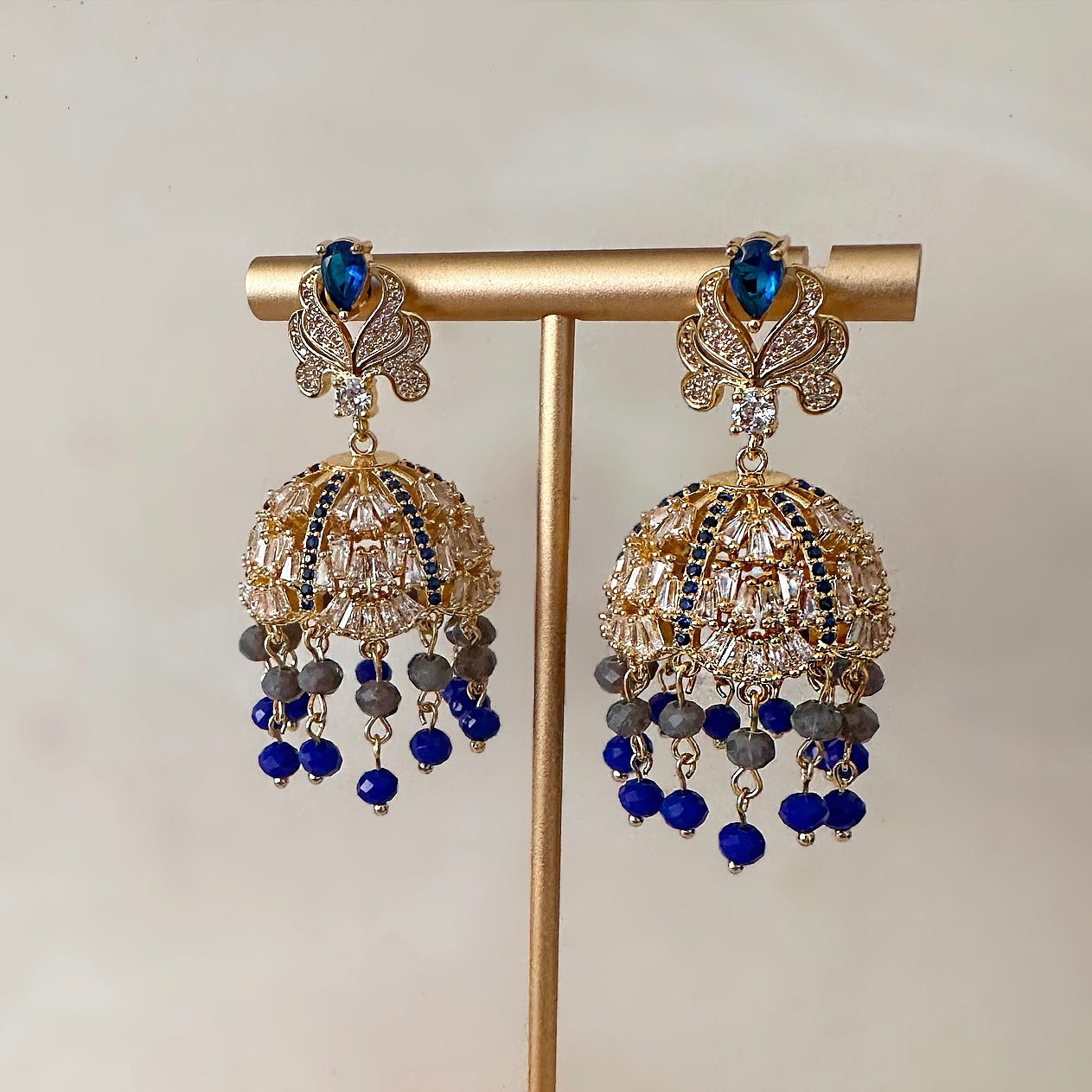 Graceful and glamorous, the Maria Blue Crystal Jhumki Earrings offer unparalleled elegance. Crafted with expert detail, these earrings sparkle with cubic zirconia and are complemented with their stunning blue grey beads for extra detail. Turn heads with their high-shine finish. Earring Drop 5cm