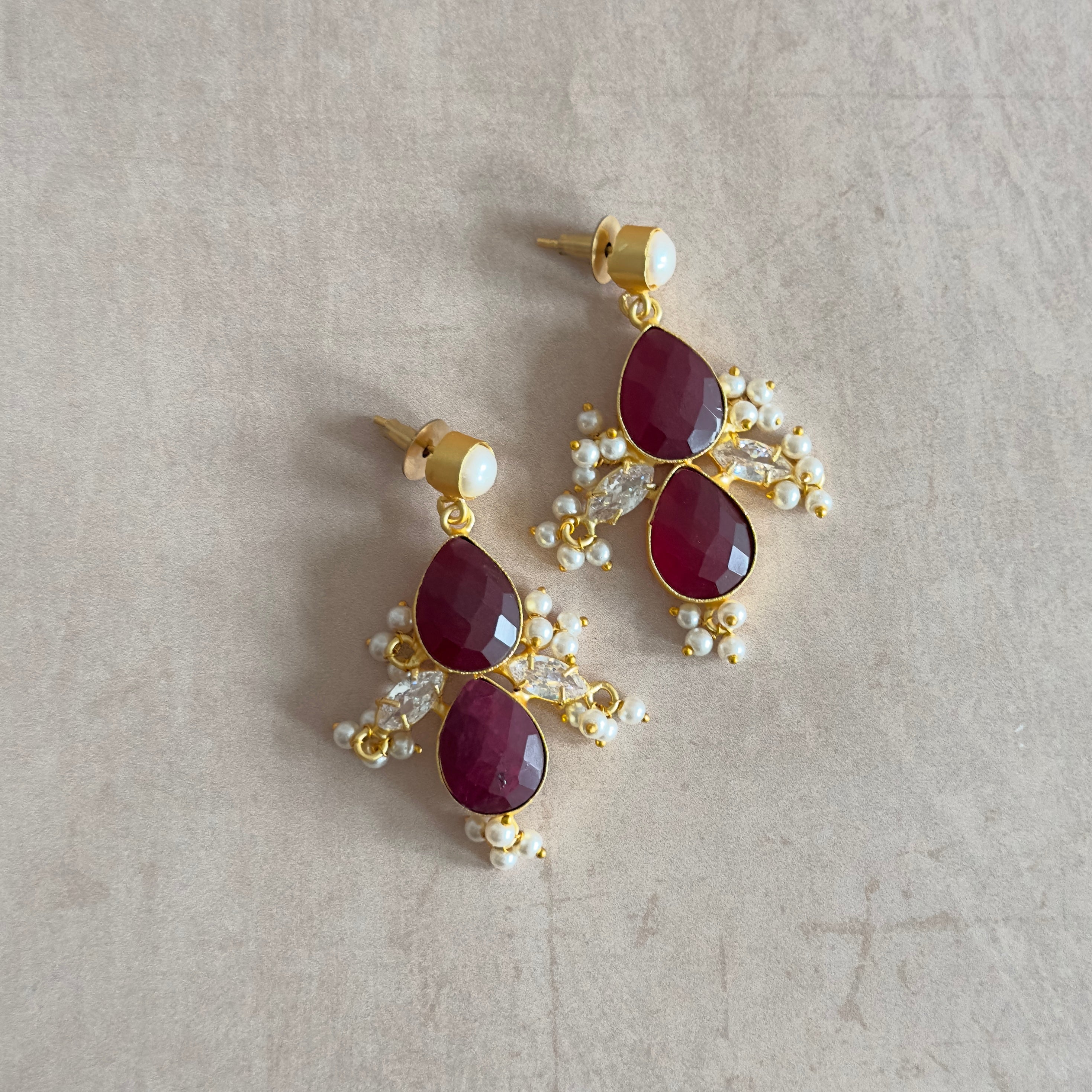 Elevate any outfit with our Maroon Pearl Drop Earrings. The deep red color of the cubic zirconia stones paired with the classic pearl accent creates a stunning and bold look. Add a touch of sophistication and glamour to your wardrobe with these elegant earrings.