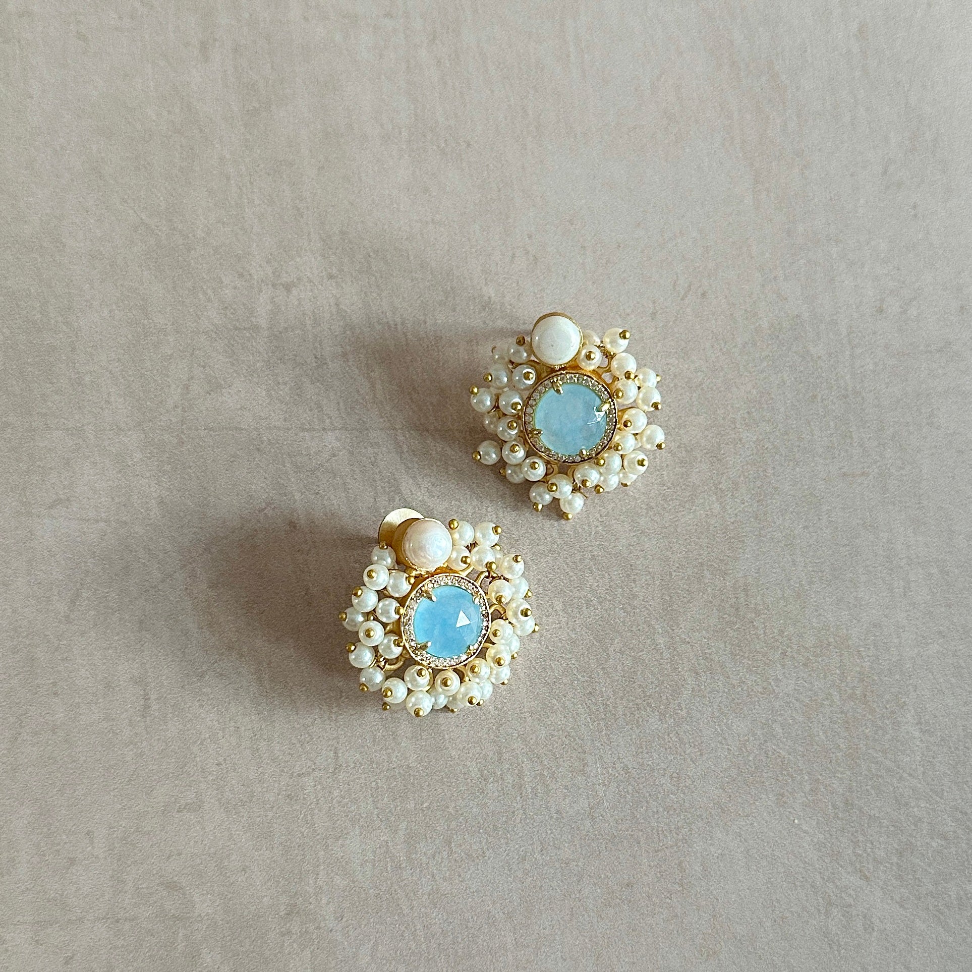 Introducing the elegant Amal Blue Stud Earrings! These classic stud earrings feature a delicate pearl accent and a stunning baby blue crystal, exuding timeless beauty and sophistication. Elevate any look with these must-have earrings.
