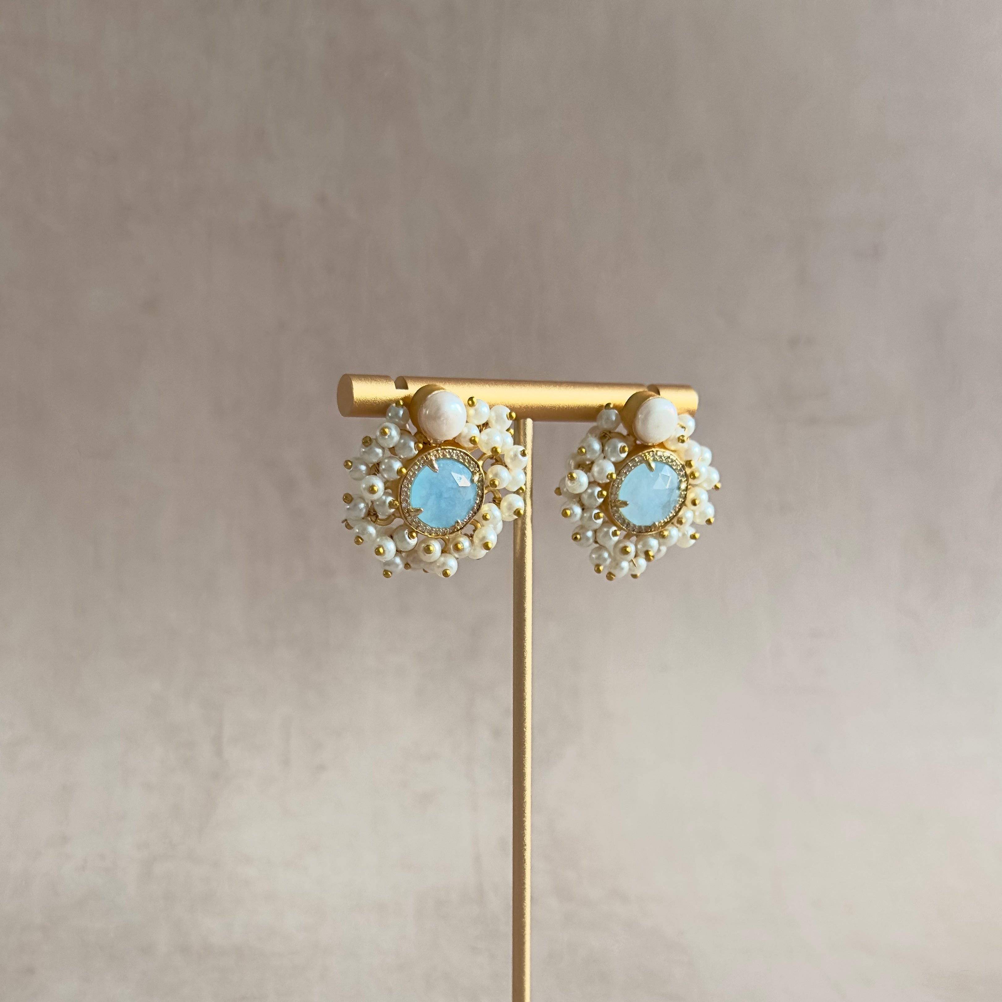 Introducing the elegant Amal Blue Stud Earrings! These classic stud earrings feature a delicate pearl accent and a stunning baby blue crystal, exuding timeless beauty and sophistication. Elevate any look with these must-have earrings.