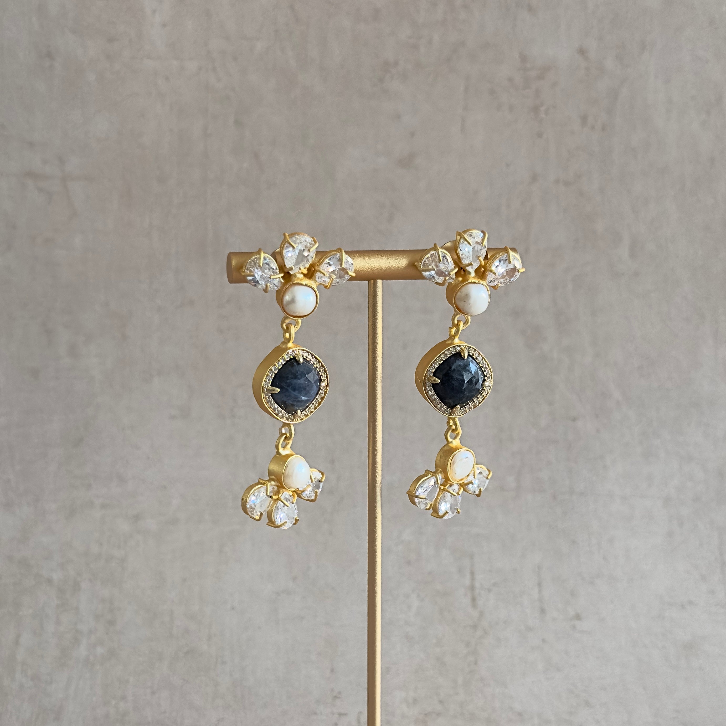 Introducing our Rifa Crystal Drop Earrings. These stunning earrings feature sparkling cz crystals and a pearl accent, complemented by a sleek black stone. Upgrade any outfit with these elegant and versatile earrings.