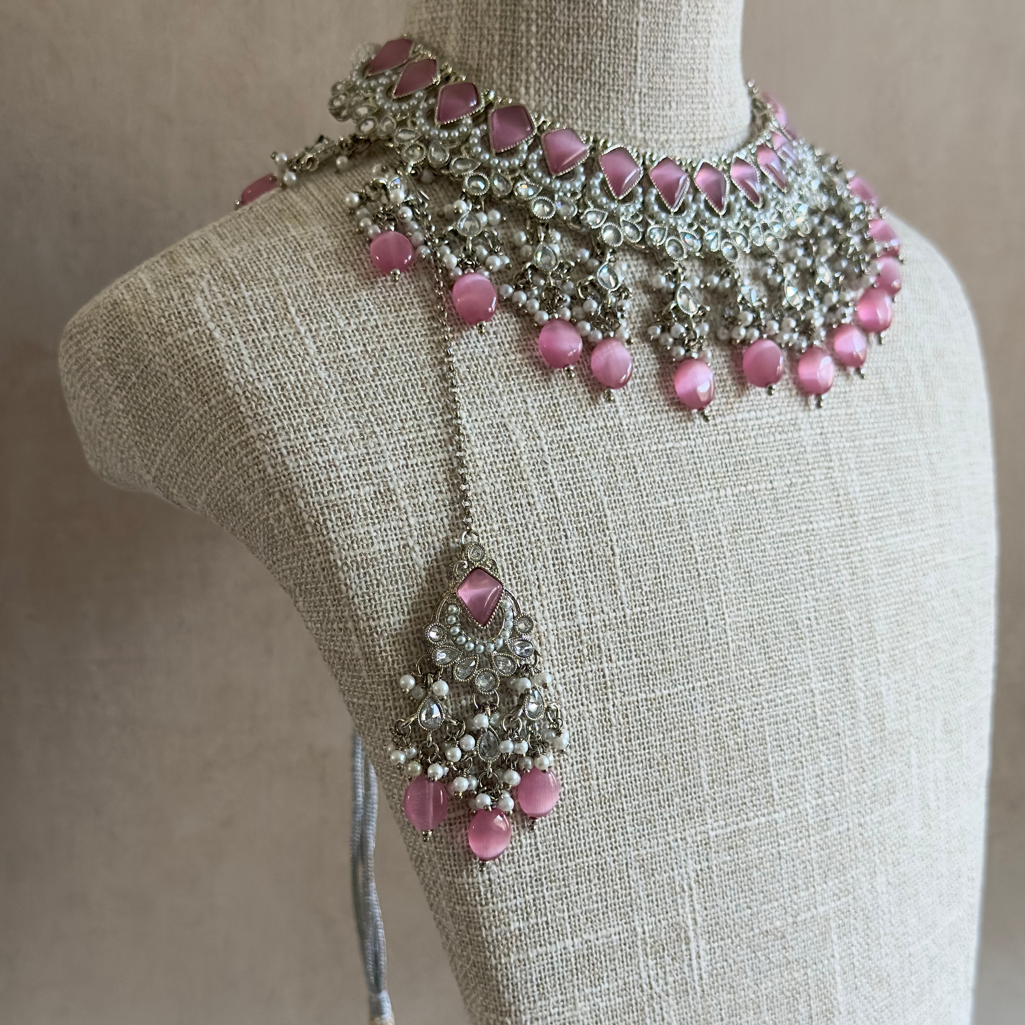 This Tessa Pink Choker Set features luscious pink cat eye stones, a sleek silver polish finish, and an adjustable fabric tie for a comfortable fit. Perfect for any formal occasion, this set also comes with matching earrings and tikka for a complete and elegant look. Elevate your style with this stunning set.