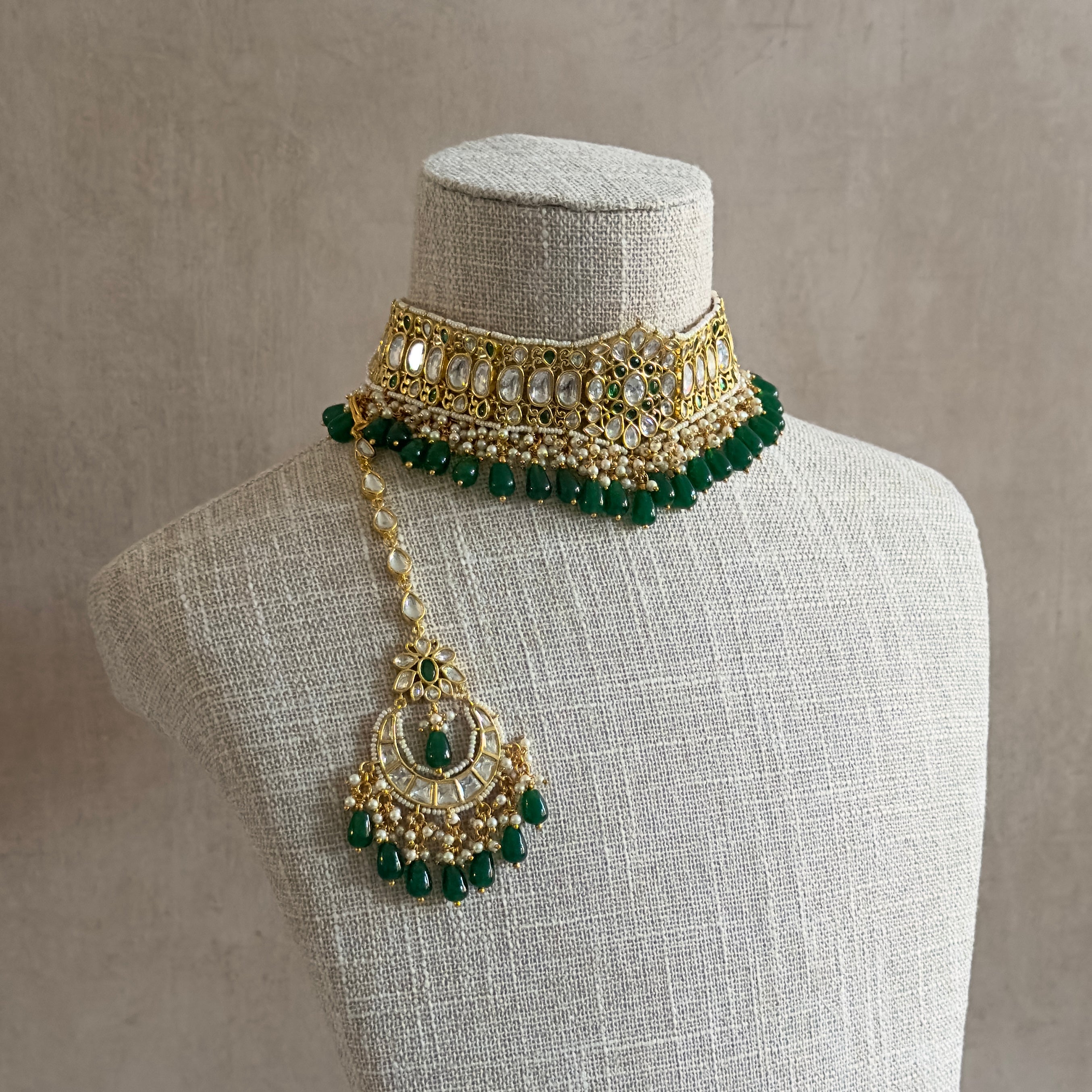This Rani Green Kundan Choker Set is nothing short of exquisite. Featuring a delicate kundan setting, lush green beads, and captivating chaandbali earrings, this set is a must-have for those who appreciate the splendor of luxurious jewelry. The matching tikka completes the look, elevating it to a higher level of opulence.
