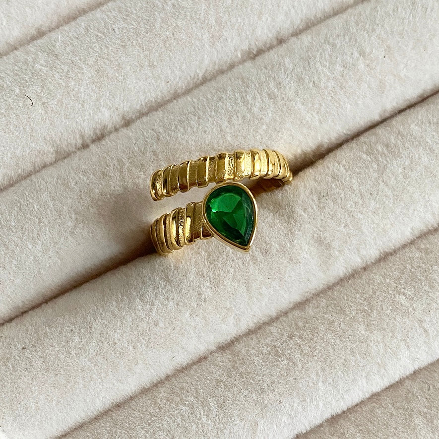 The Hold Me Tight Ring features an emerald / clear stone elegantly wrapped up in a simple and sophisticated design. Crafted with modern sophistication, this ring is sure to stand out.  18k gold plated ring. Details: Adjustable one size.