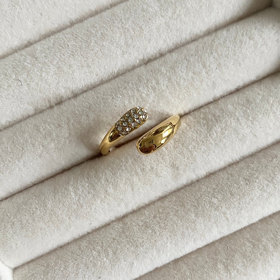 This stunning Lou Lou Gold Ring is crafted with 18k gold plating, creating a luxurious and sophisticated look. The piece is further elevated with crystal detail, adding a subtle yet eye-catching sparkle to any ensemble. A perfect accessory. Adjustable one size.